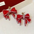 Close-up of red resin bow earrings with sparkly rhinestone borders and gold studs - Red
