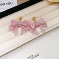 Handmade pink resin bow earrings with sparkling rhinestones on a white display tray. - Pink