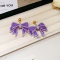 Exquisite purple resin bow earrings with sparkling rhinestones on a white jewelry tray - Purple