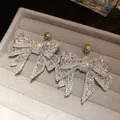 Elegant sparkling silver rhinestone bow stud earrings displayed in a grey velvet jewelry box - Silver