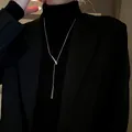 Long collier argenté en forme de goutte d'eau porté sur un pull noir à col roulé. - Collier (26)