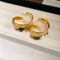Detailed close-up of chunky gold metallic wave-shaped hoop earrings on jewelry display - Gold