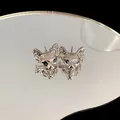Cyberpunk style silver cat head stud earrings with blue gemstone eyes displayed on mirror - Stud Earrings / Silver
