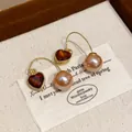 Elegant close-up of French vintage heart-shaped red gem and pink pearl drop hook earrings - Ear Hook Style / Gold Brown