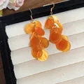 Dettaglio degli orecchini a frangia con dischi di conchiglia arancioni su un vassoio portagioie. - Stile 22#