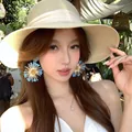 Orecchini a nappa a fiore blu e bianchi con ago d'argento indossati da modella asiatica - Grande Nappa di Fiori Radiale (Perno in Argento)