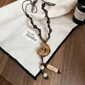 Détail d'un collier pendentif nautile ethnique avec des perles en bois sur tissu blanc - 16# Collier (HN6659-1)