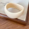 Primo piano di un bracciale in acrilico crema liscio con un design grosso e irregolare. - Bianco