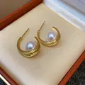 Dettaglio di eleganti orecchini a C dorati con perla centrale e pietre di zircone pavé - Orecchini a bottone a forma di C / Oro-Bianco