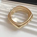 Macro detail of a chunky gold-toned acrylic geometric bangle with a glossy metallic finish. - Square / Gold