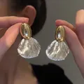 Detailed macro view of gold oval stud earrings with clear pleated shell-shaped pendants. - Minimalist Fan Embossed Style (5253742939758)