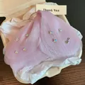 Detail view of a purple fabric flower hair claw clip with Love charm in packaging - Purple