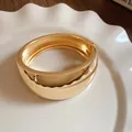 Elegante brazalete de metal dorado pulido para mujer en un plato blanco con ondas - Estilo Ensanchado De Oro Brillante (75#) / Dorado