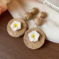 Close-up of handmade raffia earrings featuring delicate white polymer clay flowers - Brown