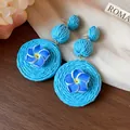 Close-up detail of blue raffia woven earrings with delicate polymer clay flowers. - Blue