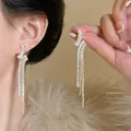 Detailed macro view of elegant silver needle zircon geometric tassel earrings on a model - Gold