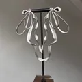 Detail view of large silver ribbon earrings with crystal accents on a display stand - Silver