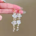 Close-up view of elegant white flower and crystal bead tassel earrings held by a hand. - Gold Style (22#)
