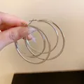 Close-up of silver multi-layer oversized hoop earrings held by hand for a detailed view. - 多层圆环(HE23342) / Silver