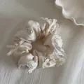 Nahaufnahme eines cremefarbenen Spitzen-Scrunchies mit Schleifen und Perlen. - Cremeweiß Mit Spitzenperlenbogen