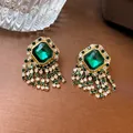 Detailed macro shot of vintage-style gold earrings with emerald green gems and rhinestone tassels. - Square Emerald Tassel Style (22#) / Green
