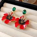 Primo piano di orecchini a fiore in smalto rosso con gemme verdi e cristalli brillanti. - Forma di Fiore / Perno per orecchini in argento - Rosso