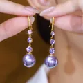 Close-up of elegant gold drop earrings with purple stones and pearls held by hand. - 5# Hook
