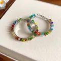 Close-up detail of stylish colorful crystal beaded hoop earrings on a soft beige mat. - Silver Multicolor