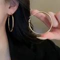 Macro view of gold oval hoop earrings with silver needles being held to show size scale - Large Oval Hoop Style (37) / Diameter 60mm / Gold
