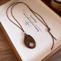 Détail du collier avec pendentif ovale en résine marron sur un plateau en bois - Café