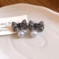Close-up detail of vintage pleated silver bow earrings with elegant grey pearl drops - Black