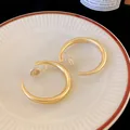 Dettaglio ravvicinato di orecchini a clip a forma di C in oro opaco su un piatto di porcellana - Orecchini a clip / Oro