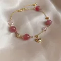 Detailed macro view of synthetic strawberry quartz beads and gold heart charm bracelet - Heart Style