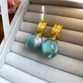 Close-up of teal resin ball earrings with gold geometric studs in a tray - Gold Irregular Geometric Style / Green