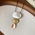 Macro detail of three-tone metallic geometric pendants on a minimalist black cord necklace. - Gold, Silver, Rose Gold