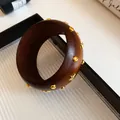 Macro view of a chunky dark brown acrylic bangle decorated with gold star and round studs. - Wood Grain Rivet Star Bangle / Coffee/Gold