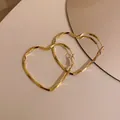 Close-up detail of golden heart-shaped twisted hoop earrings on a light background - Large Heart Twisted (HE8275) / Gold