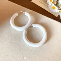 Detailed view of minimalist white acrylic C-shaped hoop earrings on a soft beige surface - White