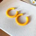 Close-up of bright yellow C-shaped acrylic earrings on a textured white surface - Yellow