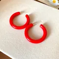 Close-up of vibrant red acrylic C-shaped hoop earrings with silver pins on a beige display pad. - Red