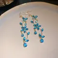 Detailed shot of sparkling blue zircon butterfly and flower tassel hook earrings in gold. - Butterfly Flower Tassel Style / Blue