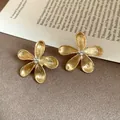 Detailed macro view of golden five-petal flower stud earrings with pearl centers - Flower Style (HE30410) / Gold