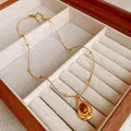 Gros plan d'un collier doré avec pendentif ovale en œil de tigre dans un coffret - Pendentif Goutte