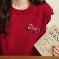 Close-up detail of a cute red embroidered horse brooch pinned on a stylish red knitted vest - Red Embroidered Style / Red
