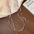 Elegant long pink pearl sweater chain with teardrop crystal pendants on silk background. - Necklace / Purple