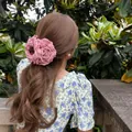 Rückansicht einer Frau mit einer großen rosa Stoffrose-Haarklammer in einem schönen Garten - Rosa Kamelie (Große Kralle)