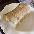 Detailed view of wide gold cuff bracelet with intricate embossed floral patterns - Gold