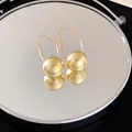 Macro view of gold sphere drop earrings featuring unique radial texture and hook design. - Gold