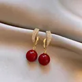 Close-up of golden geometric earrings with pavé zircons and red spherical drops. - Silver Earring Post Style / Gold-Red