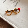 Detailed close-up of a trendy acrylic glasses-shaped hair clip with a red apple accent. - Glasses and Apple Design / Amber